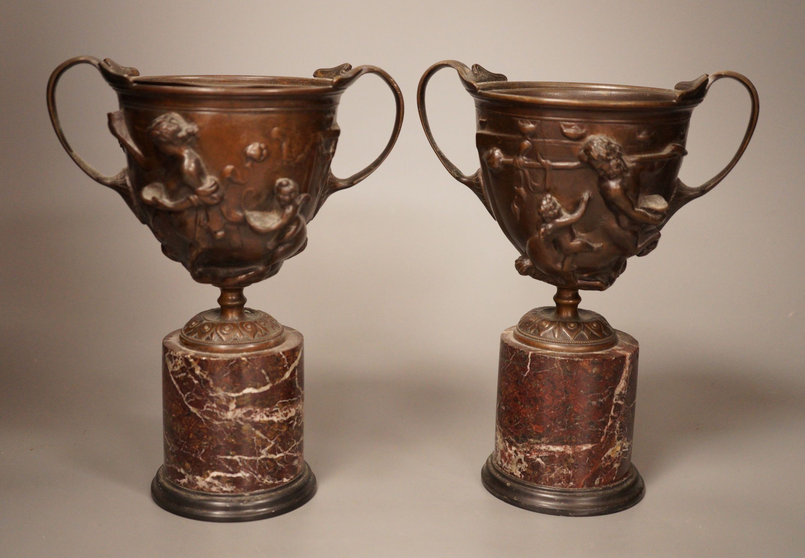 A pair of early 20th century twin handled bronze cups on marble plinth bases, 22cm